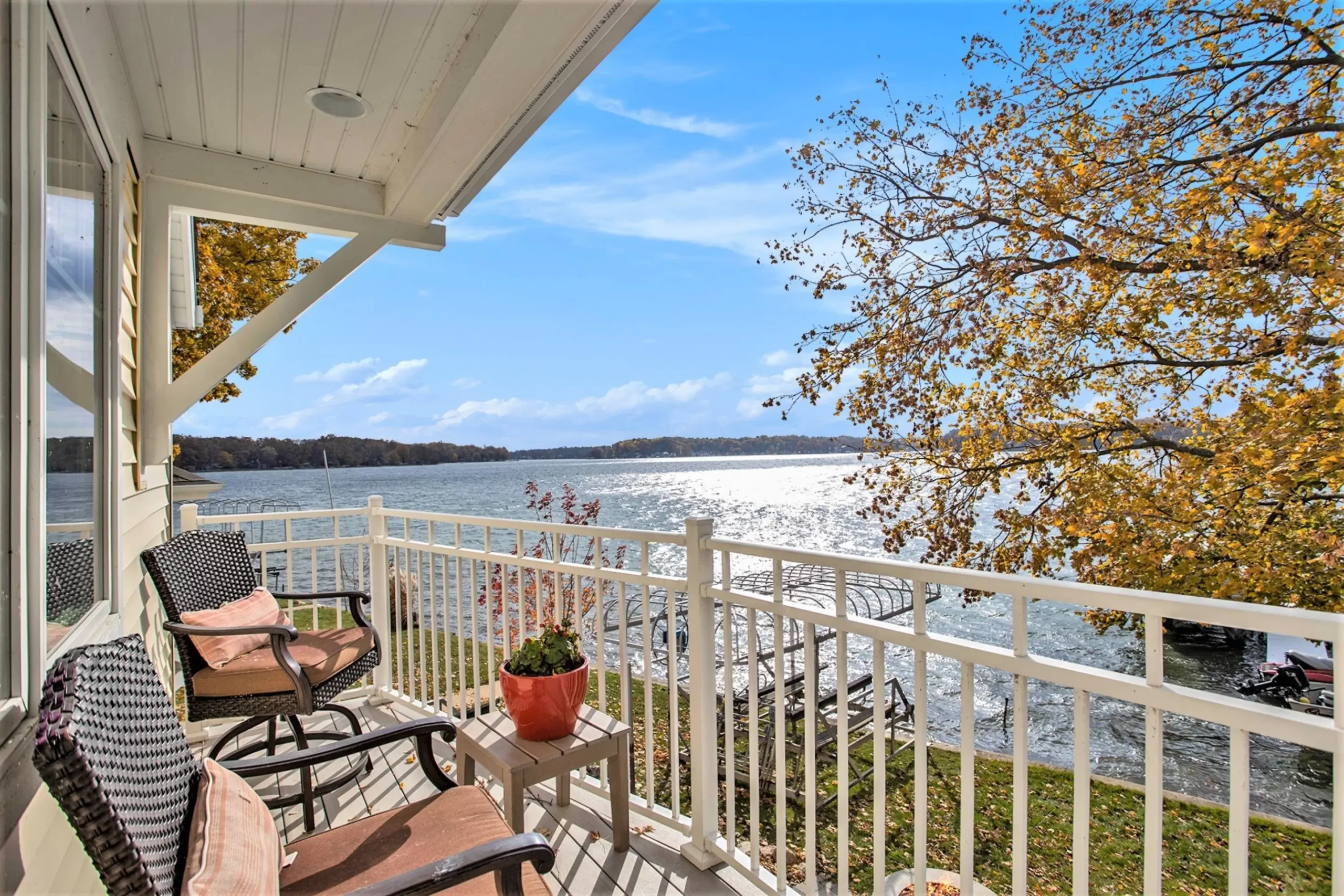 Covered balcony with outdoor seating overlooking the lake, docks, and colorful autumn trees