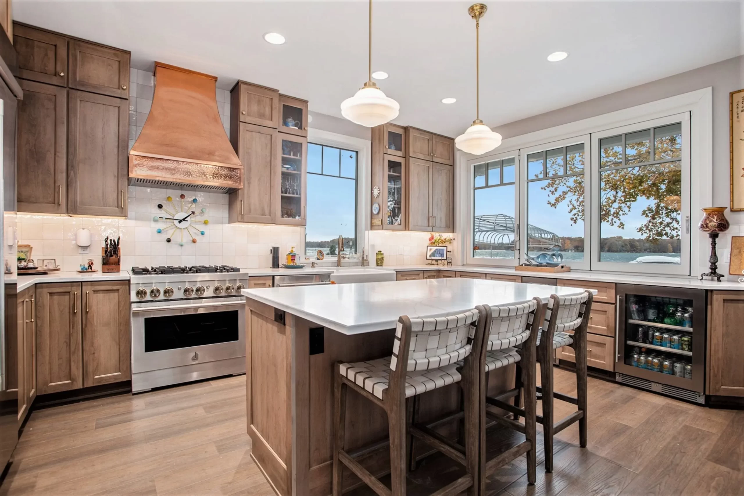 Custom kitchen with large island, copper range hood, paneled cabinetry, pendant lights, and lake views through wide windows
