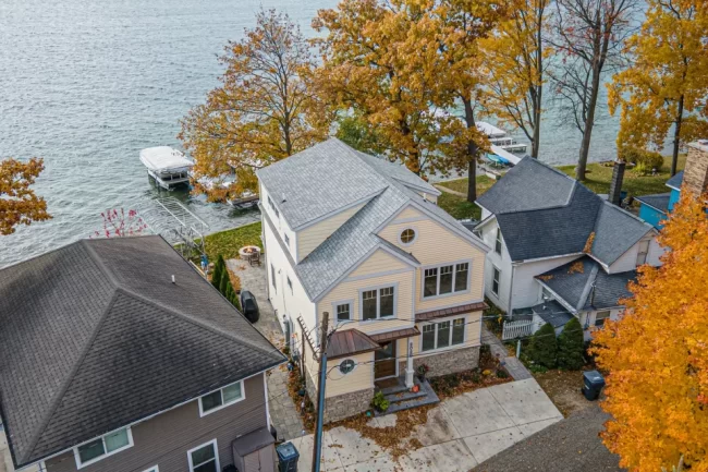 Aerial View of Lakefront Custom Home | Pennings & Sons Aerial view of a lakefront custom home with waterfront lawn, dock access, mature trees, and neighboring cottages