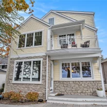 Lakeside exterior of a lakefront home with stone accents, upper balcony, patio area, and large windows