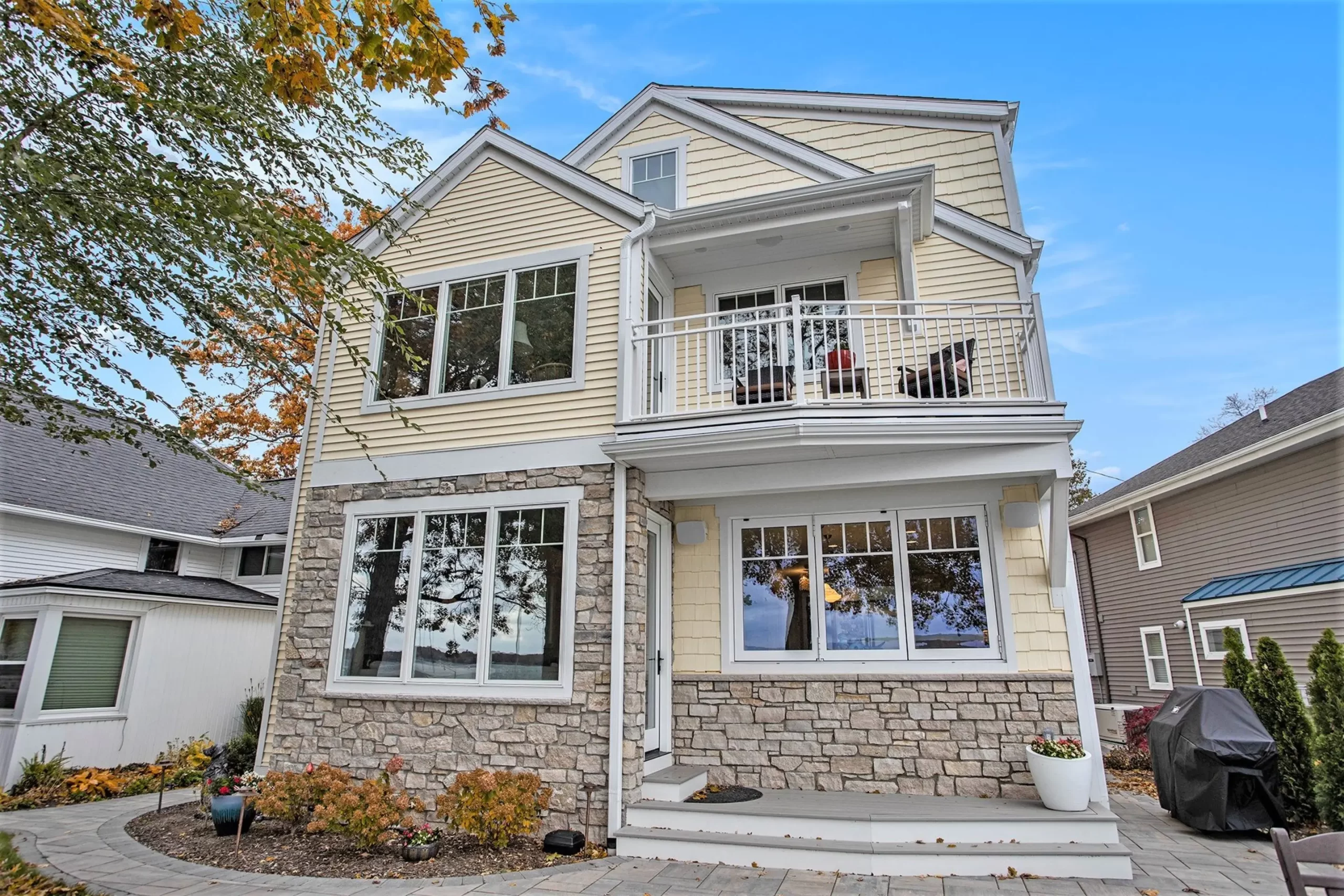 Lakeside exterior of a lakefront home with stone accents, upper balcony, patio area, and large windows