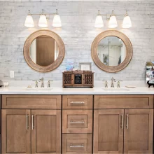 Double vanity with custom wood cabinetry, polished fixtures, two round mirrors, bright lighting, and tile backsplash