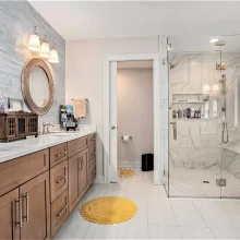 Primary bathroom with double wood vanity, round mirrors, glass walk-in shower, marble-look tile, and light flooring