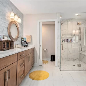 Primary bathroom with double wood vanity, round mirrors, glass walk-in shower, marble-look tile, and light flooring