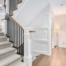 Stair landing with white borad and batten wall pattern, black balusters, wood handrail, hardwood flooring, and bright hallway lighting