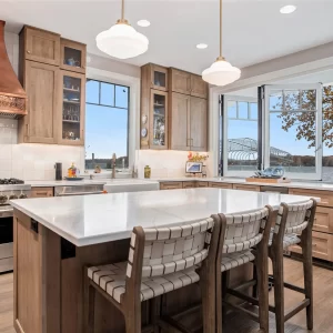 Waterfront kitchen with folding pass-through window, large island, copper hood, wood cabinets, beverage fridge, and lake view