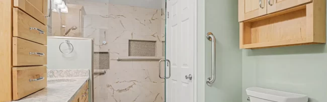 Accessible Bathroom Remodel with Walk-In Shower | Pennings & Sons Accessible bathroom remodel with walk-in shower, glass door, grab bars, double vanity, and light wood cabinetry