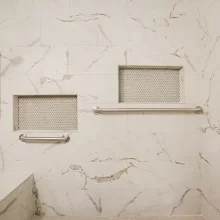 Marble-look tiled shower with recessed storage niches, safety grab bars, built-in bench, and handheld shower head