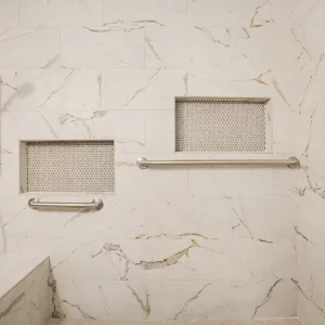 Marble-look tiled shower with recessed storage niches, safety grab bars, built-in bench, and handheld shower head