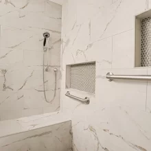 Accessible tile shower with grab bars, recessed storage niches, handheld shower head, and built-in bench