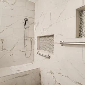 Accessible tile shower with grab bars, recessed storage niches, handheld shower head, and built-in bench