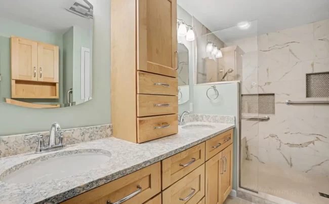Custom Double Vanity with Accessible Shower | Pennings & Sons Custom bathroom vanity with light wood cabinets, granite-style countertop, mirrors, and accessible tiled shower