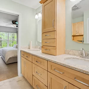 Primary bathroom remodel with double sinks, light wood cabinetry, granite-style countertop, and wall-mounted mirrors