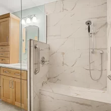 Walk-in tiled shower with built-in bench, handheld shower head, grab bars, glass enclosure, and recessed niche