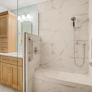 Walk-in tiled shower with built-in bench, handheld shower head, grab bars, glass enclosure, and recessed niche
