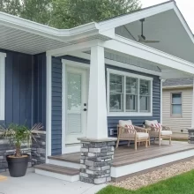Covered Lakeside porch with blue siding, white columns, stone column bases, wood porch decking, outdoor seating, and landscaped yard