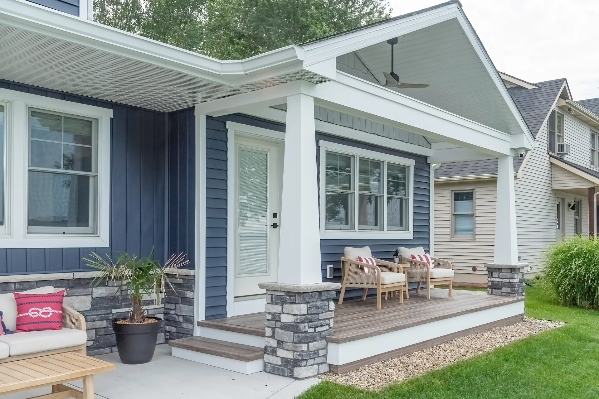 Covered Lakeside porch with blue siding, white columns, stone column bases, wood porch decking, outdoor seating, and landscaped yard