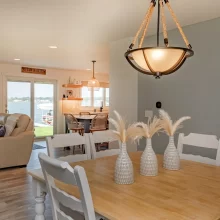 Dining area with white chairs, wood table, pendant light, lake views, and open sightline to the living room and kitchen