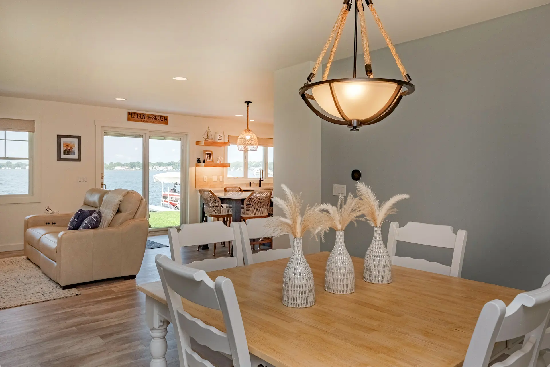 Dining area with white chairs, wood table, pendant light, lake views, and open sightline to the living room and kitchen