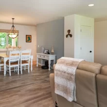 Open dining and living area with white dining table, pendant light, neutral seating, wood-look flooring, and bright natural light