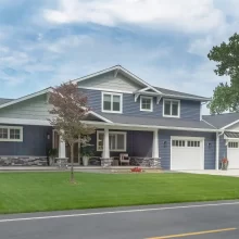 Front view of a Portage Austin Lake home with blue siding, covered porch, white garage doors, stone columns, and manicured lawn