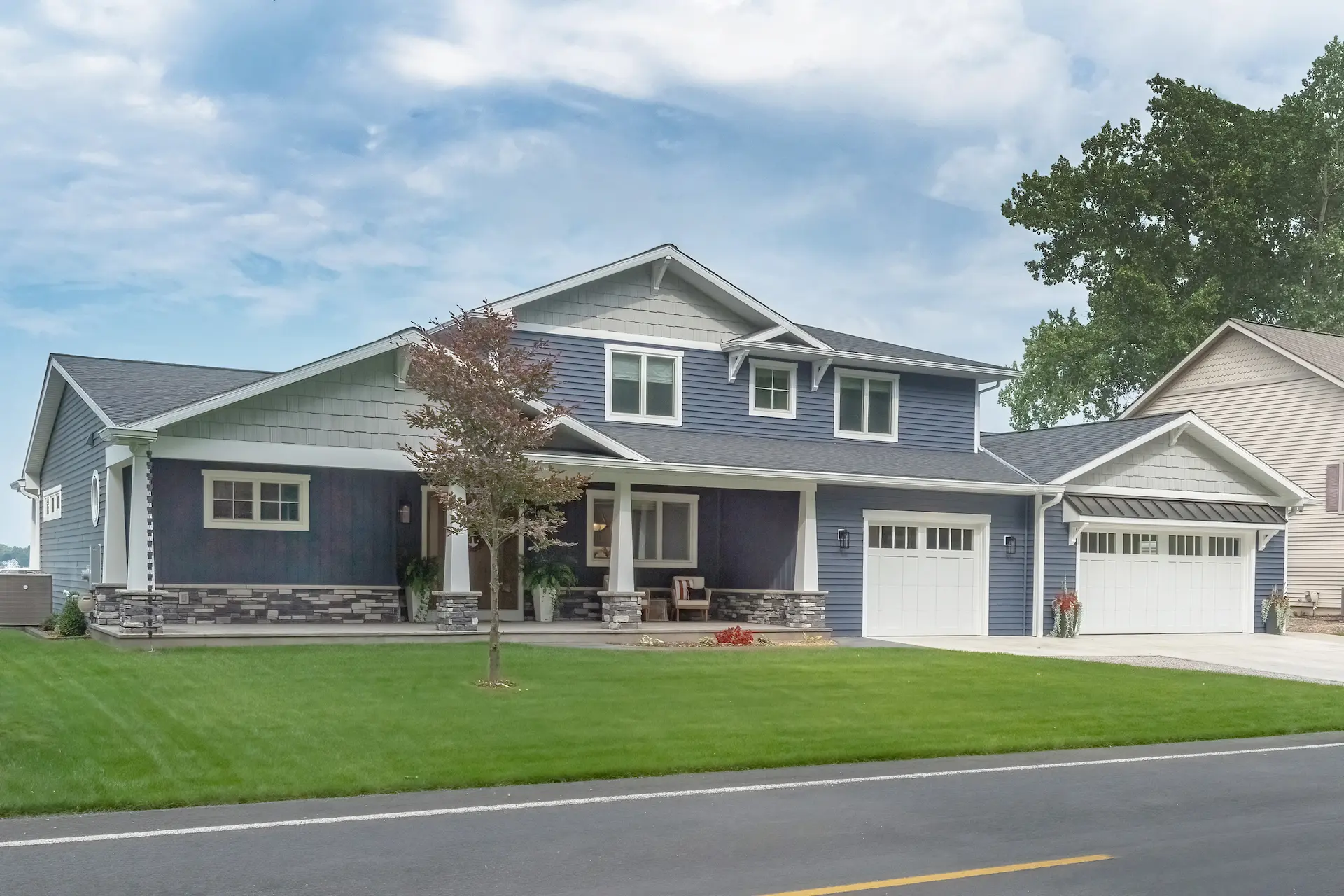Front view of a Portage Austin Lake home with blue siding, covered porch, white garage doors, stone columns, and manicured lawn