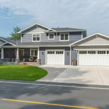 Front exterior of a Portage Austin Lake home with blue siding, white garage doors, covered porch, stone accents, and landscaped lawn