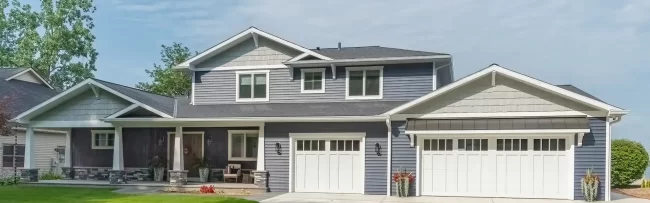 Front exterior of a Portage Austin Lake home with blue siding, white garage doors, covered porch, stone accents, and landscaped lawn