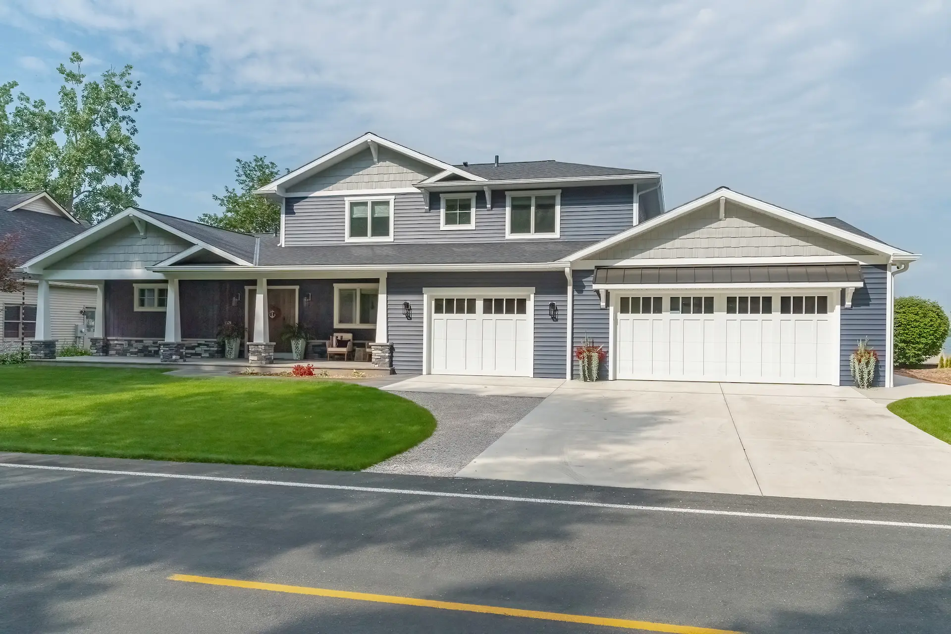 Front exterior of a Portage Austin Lake home with blue siding, white garage doors, covered porch, stone accents, and landscaped lawn