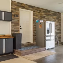 Finished garage entry area with stone accent wall, raised platform, exterior door, storage cabinets, refrigerator, and concrete floor