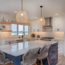 Custom kitchen with blue island, white cabinetry, woven pendant lights, lake-facing windows, tile backsplash, and open shelving