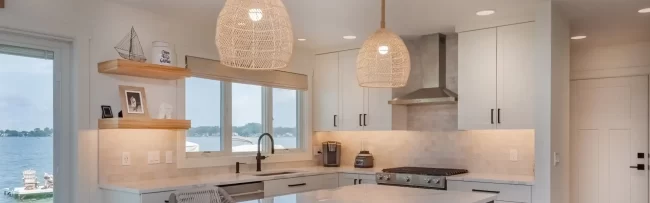 Custom kitchen with blue island, white cabinetry, woven pendant lights, lake-facing windows, tile backsplash, and open shelving