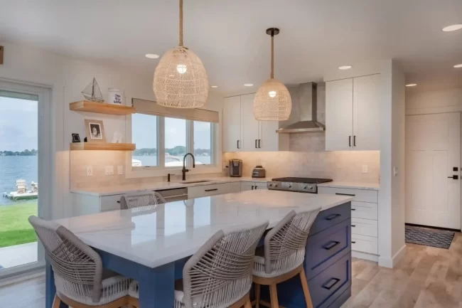 Custom kitchen with blue island, white cabinetry, woven pendant lights, lake-facing windows, tile backsplash, and open shelving