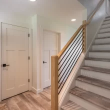 Interior staircase with wood handrail, black metal balusters, white doors, wood-look flooring, and clean modern trim details