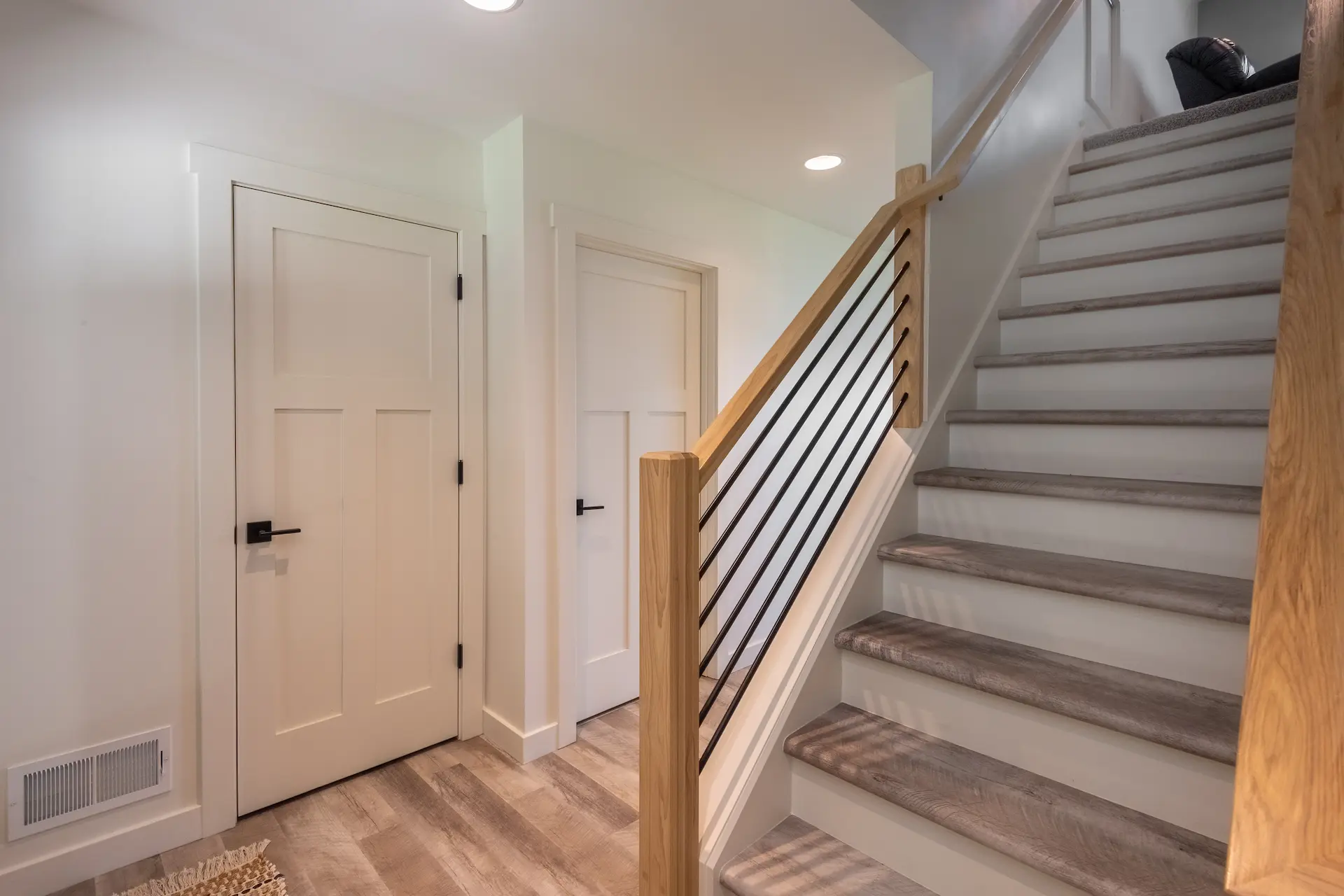 Interior staircase with wood handrail, black metal balusters, white doors, wood-look flooring, and clean modern trim details