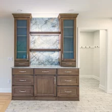 Floor to ceiling darker wood cabinet with marble backing attached to the wall in between living room and kitchen to be used as a dry bar