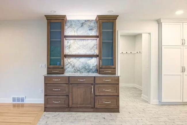 Floor to ceiling darker wood cabinet with marble backing attached to the wall in between living room and kitchen to be used as a dry bar