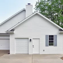 New garage addition extending out from the house facing North showing half size overhead door with side service door and window with gray shutters