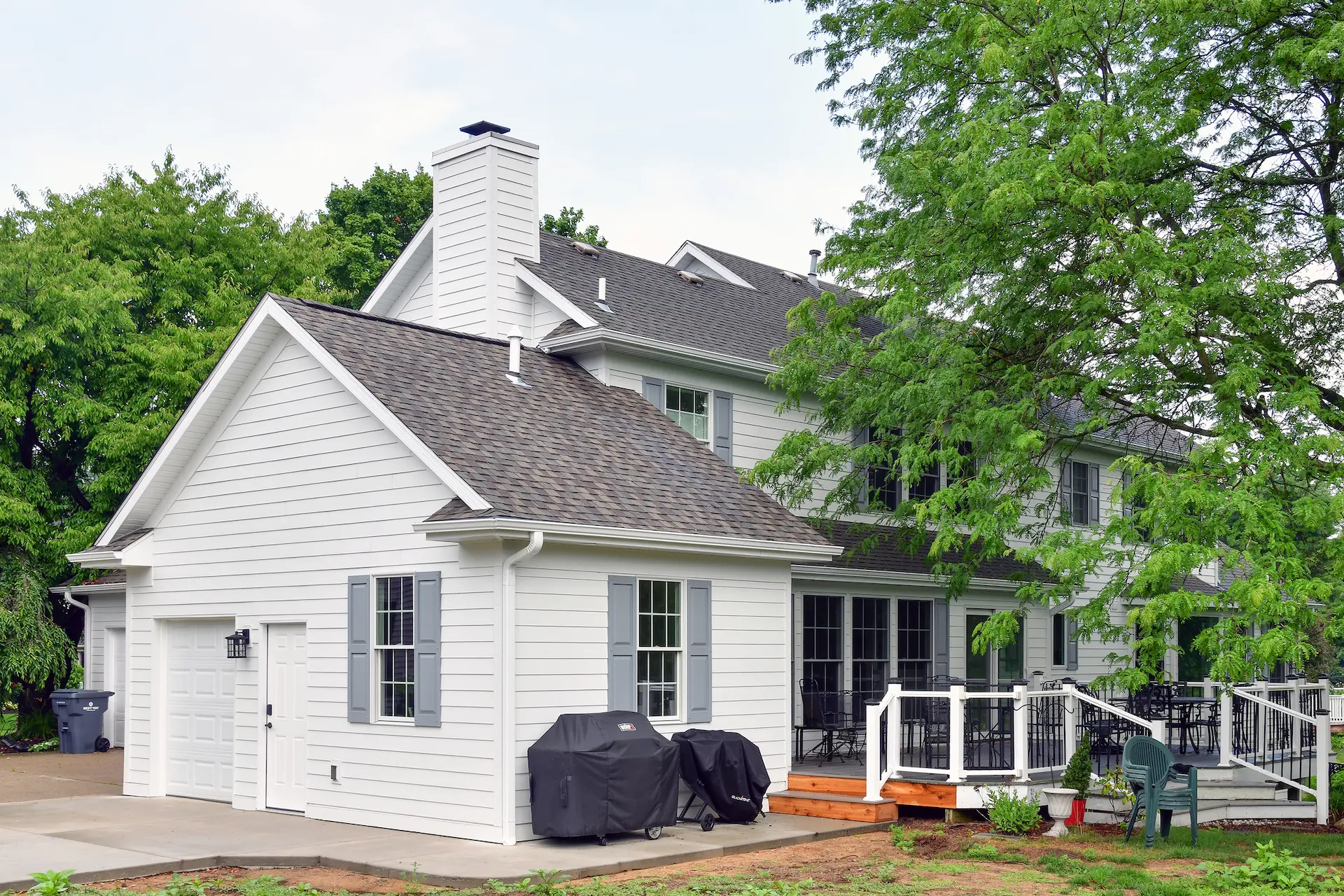 New garage addition extending out from the house facing North showing half size overhead door with side service door and two windows with gray shutters