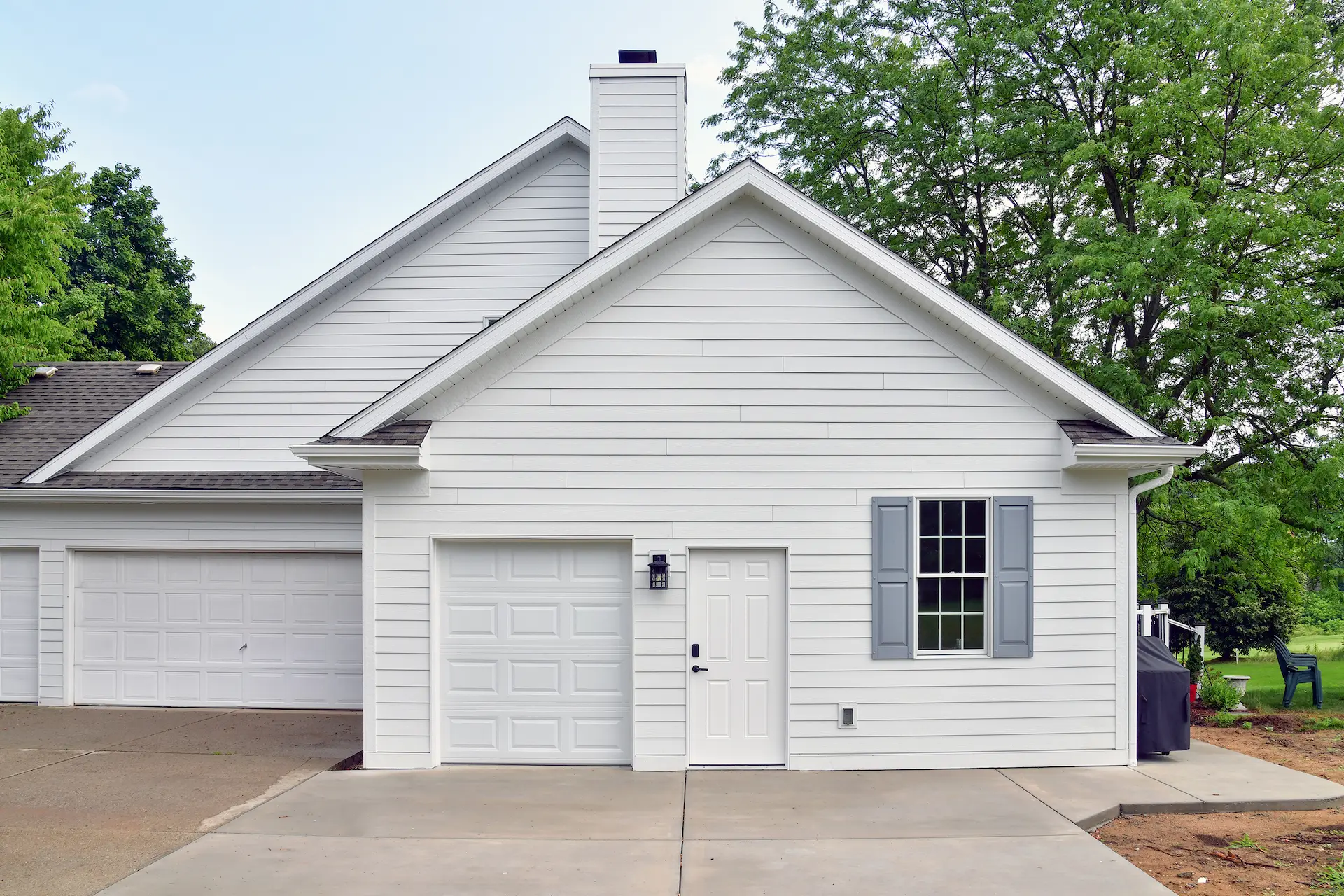 New garage addition extending out from the house facing North showing half size overhead door with side service door and window with gray shutters