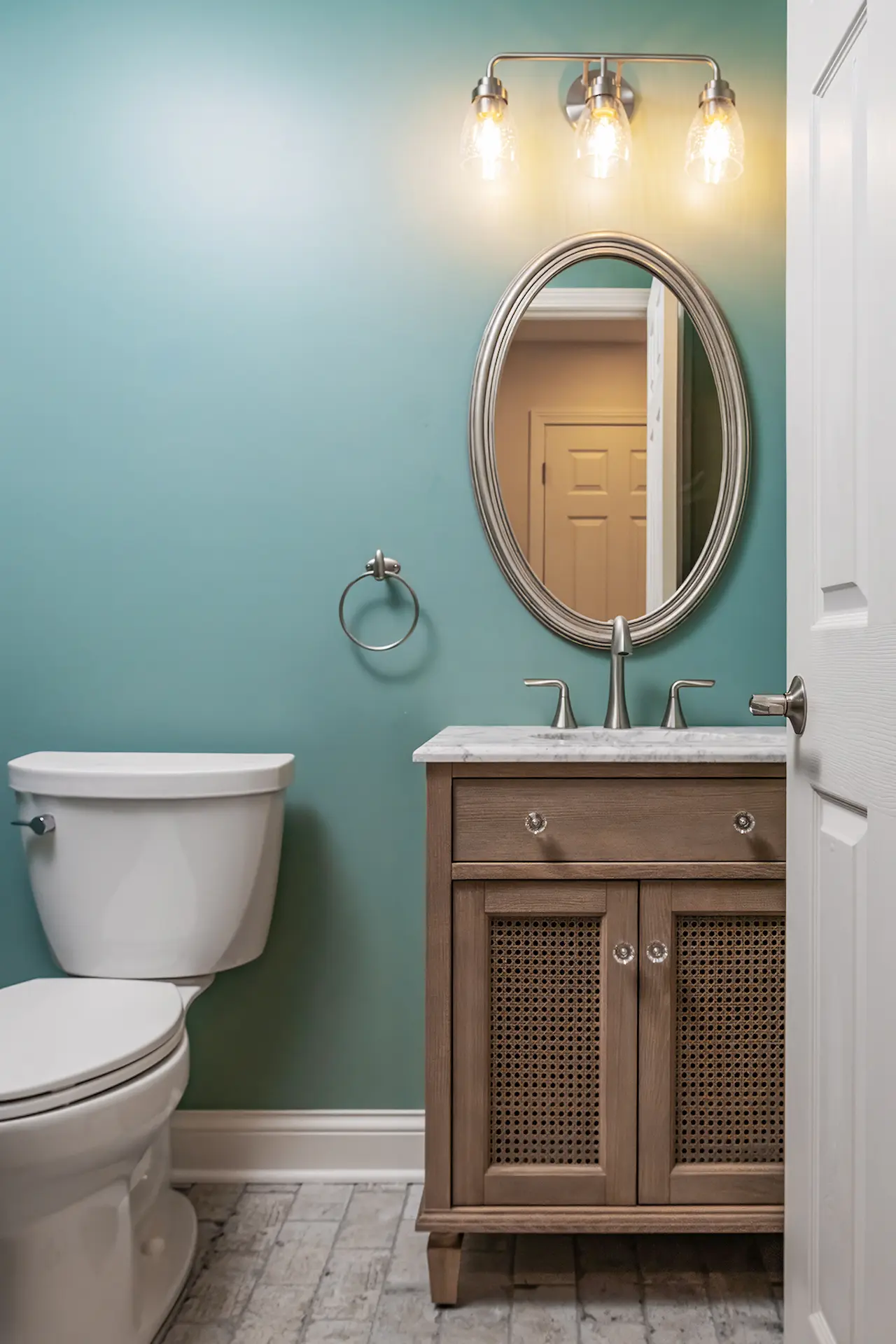 New light flooring that matches Kitchen in a light colored brick design, with small single sink vanity with oval mirror on wall above sink with white toilet to the left of the sink