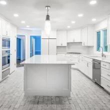 Kitchen with all white cabinets and island in the middle with matching brick shaped backsplash and flooring