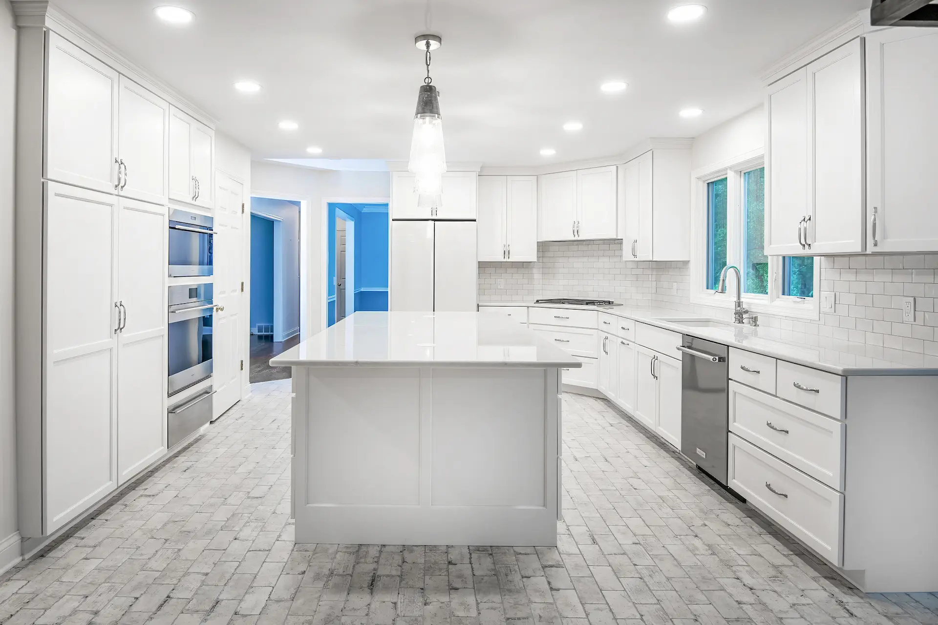 Kitchen with all white cabinets and island in the middle with matching brick shaped backsplash and flooring