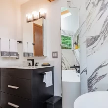 Modern bathroom vanity with black cabinetry, wall mirror, black fixtures, towel bars, freestanding tub, and concealed storage pane