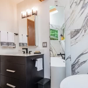 Modern bathroom vanity with black cabinetry, wall mirror, black fixtures, towel bars, freestanding tub, and concealed storage pane