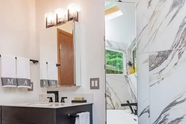 Modern bathroom vanity with black cabinetry, wall mirror, black fixtures, towel bars, freestanding tub, and concealed storage pane