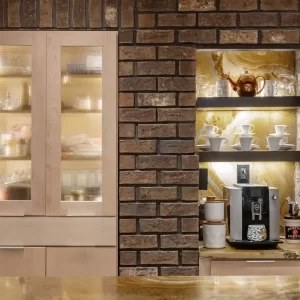 Built-in coffee bar set into a brick wall with lighted shelves, textured glass cabinet doors, coffee maker, cups, and stone countertop