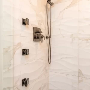 Custom shower with marble-look wall tile, handheld shower, rain showerhead, body sprays, black fixtures, and gray tile floor