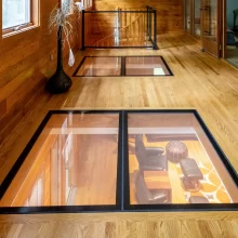 Long wood-paneled hallway with glass floor panels, windows, decorative floor vase, and railing around the stair opening