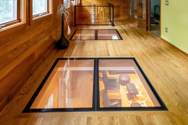 Loft Hallway with Glass Panels in Floor | Pennings & Sons Long wood-paneled hallway with glass floor panels, windows, decorative floor vase, and railing around the stair opening